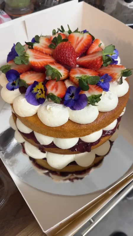 Homemade layered sponge cake topped with fresh strawberries, whipped cream rosettes and purple edible pansies