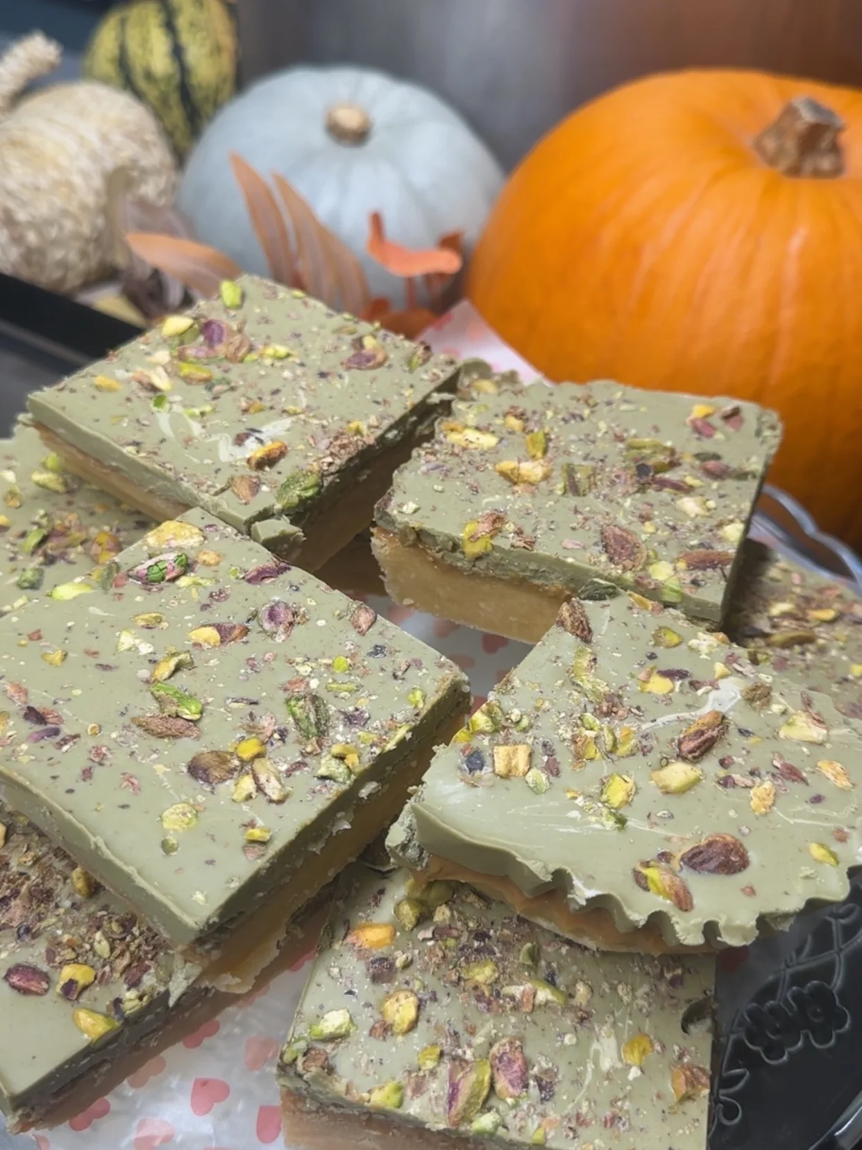 Homemade pistachio and chocolate Dubai cake traybake squares with autumn pumpkins in the background